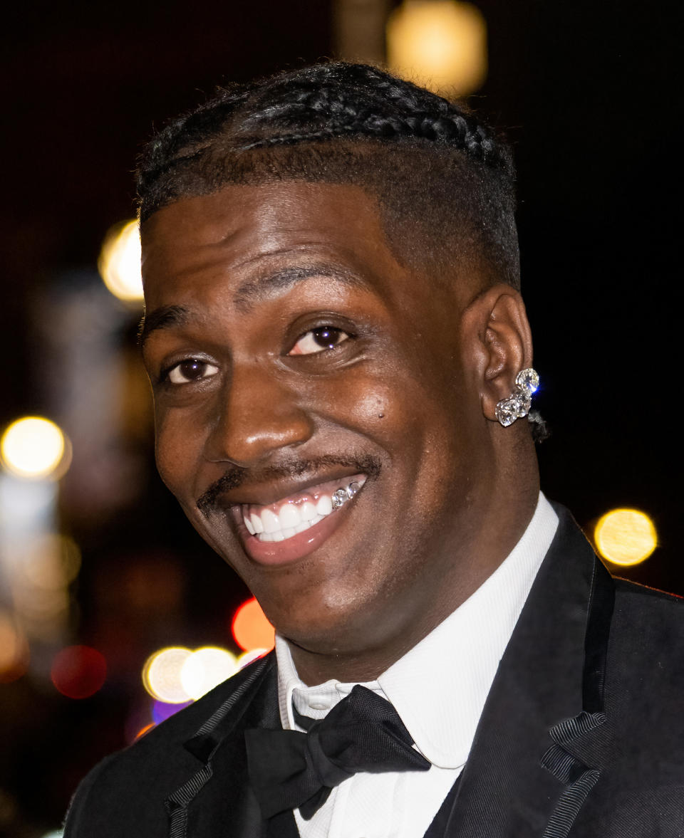 Smiling man wearing a tuxedo, braided hair and diamond-studded earrings