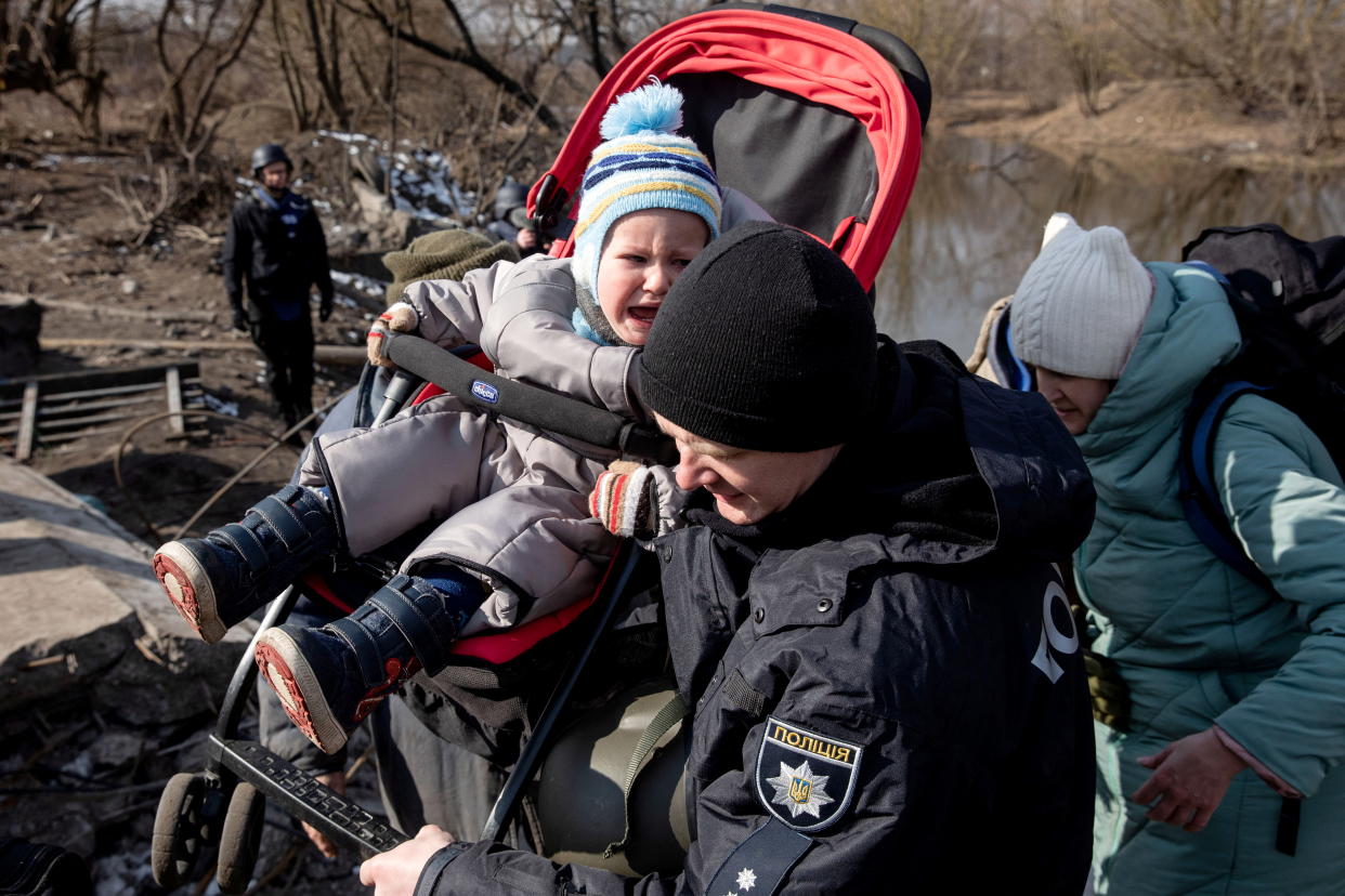 A baby is carried as people flee near a destroyed bridge to cross Irpin River as Russia's invasion on Ukraine continues, in Irpin outside Kyiv, Ukraine, March 9, 2022. REUTERS/Mikhail Palinchak