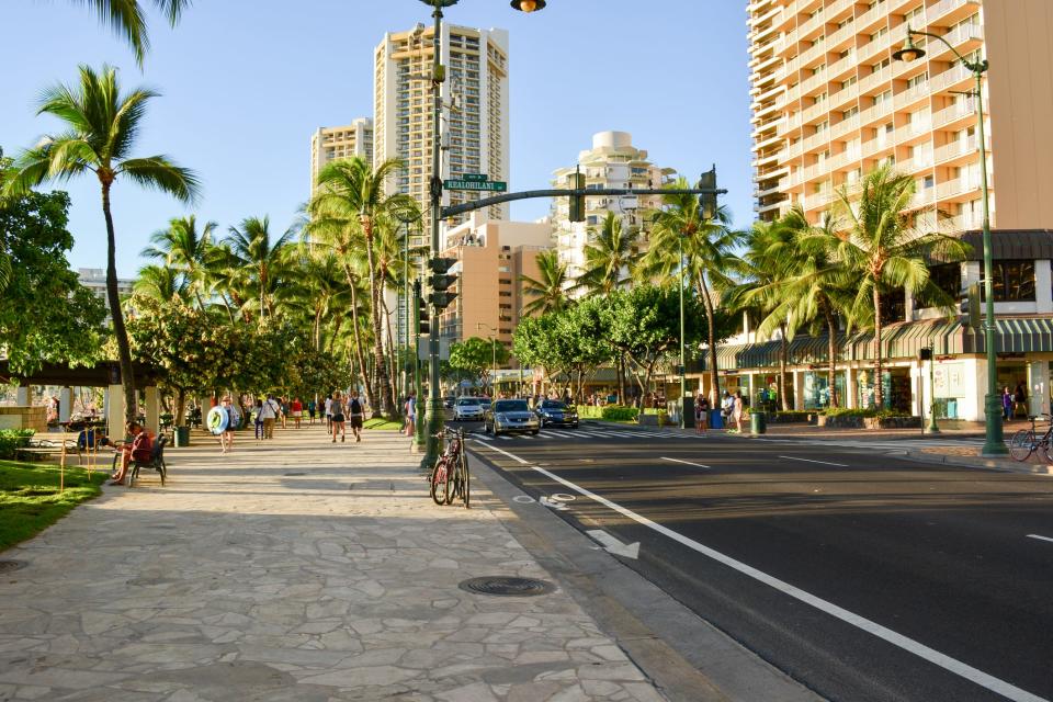 Many people walk down Waikiki strip, which is full of shops and restaurants.