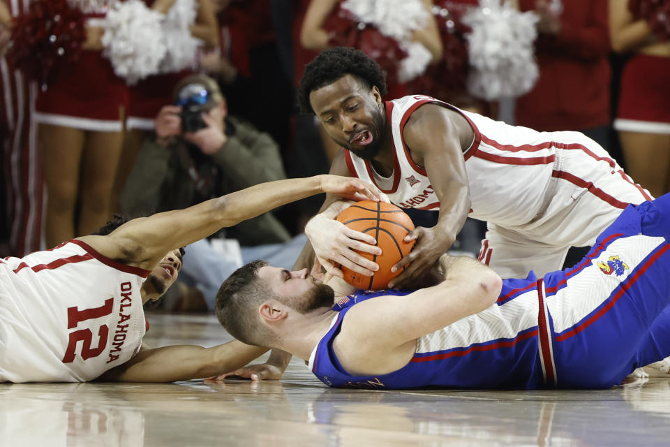 Kansas center Hunter Dickinson, center, fights for the ball with Oklahoma guard Milos Uzan (12) and guard Le'Tre Darthard, top, during the first half of an NCAA college basketball game Saturday, Feb. 17, 2024, in Norman, Okla. (AP Photo/Garett Fisbeck)