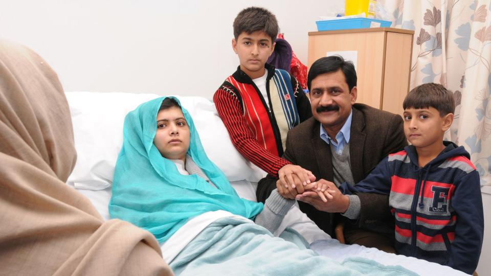 malala yousafzai lies in a hospital bed as her father and two younger brothers hold her hand from the side of the bed