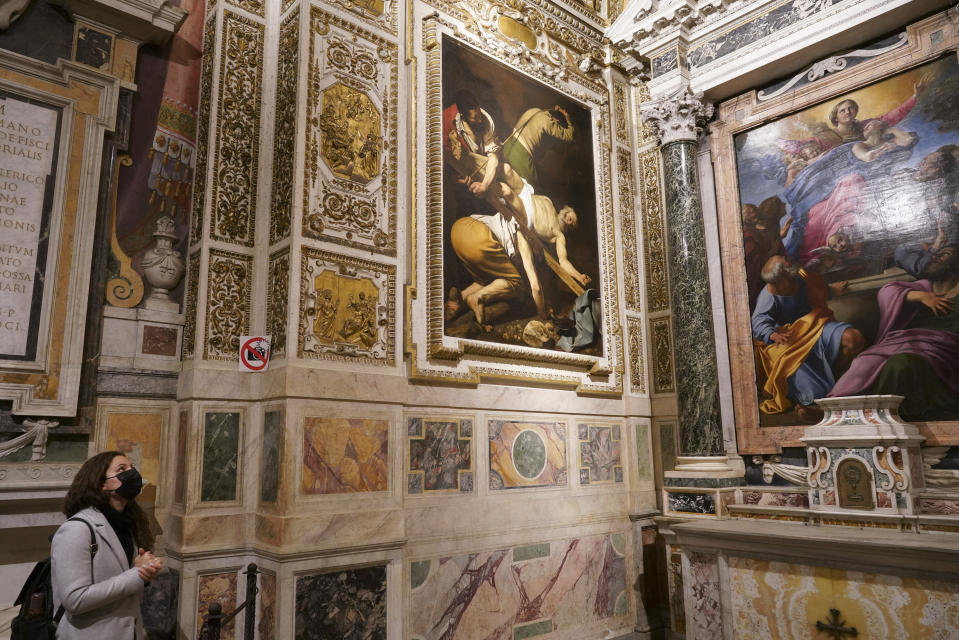 A woman wearing a face mask to curb the spread of COVID-19 admires paintings he Cerasi Chapel of Santa Maria del Popolo church, Rome, Friday, Dec. 11, 2020. At left is "The Crucifixion of St. Peter", 1601, by Renaissance master Michelangelo Merisi, known as Caravaggio, and at right, "The Assumption of the Virgin", 1601, by Annibale Carracci. Like elsewhere in Europe, museums and art galleries in Italy were closed this fall to contain the spread of COVID-19, meaning art lovers must rely on virtual tours to catch a glimpse of the treasures held by famous institutions such as the Uffizi in Florence and the Vatican Museums in Rome. However, some exquisite gems of Italy's cultural heritage remain on display in real life inside the country's churches, some of which have collections of renaissance art and iconography that would be the envy of any museum. (AP Photo/Andrew Medichini)