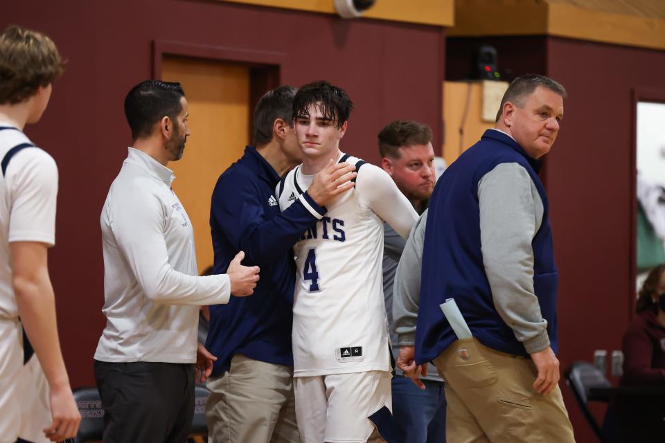 As head coach David Morissette looks toward the floor, St. Thomas Aquinas' Brady Rogers (4) is consoled by teammates after Wednesday's 62-49 loss to Mascoma in a Division III boys basketball semifinal at Goffstown High School.