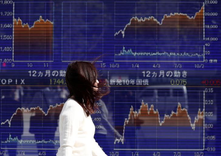 A woman walks in strong wind caused by Typhoon Lan, past an electronic board showing the graphs of the recent movements of Japan's Nikkei average outside a brokerage in Tokyo, Japan, October 23, 2017. REUTERS/Issei Kato