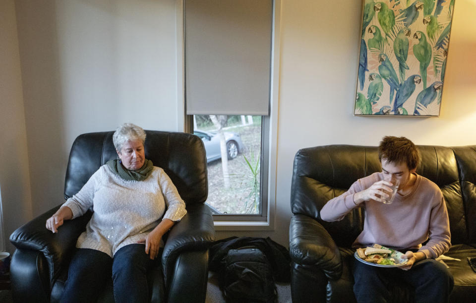 Sam Ware, 22, eats as his mother, Deb Ware, sits by, upon letting him return to her home for the first time since he last overdosed, in Fountaindale, Central Coast, Australia, Friday, July 19, 2019. Deb lets Sam inside, into the warmth of the living room. He sits on the couch where he overdosed three weeks earlier and wolfs down a sandwich, and toast, and cereal, and cookies. Deb sinks into her armchair, looking broken. (AP Photo/David Goldman)