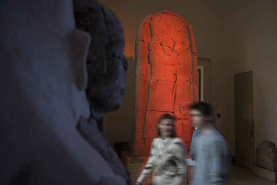 Visitors pass the Victory stele of Esarhaddon illuminated by artist Liam Gillick during a press preview for his exhibition Filtered Time at Pergamon Museum in Berlin, Tuesday, April 4, 2023. A new light and sound installation by British contemporary artist Liam Gillick, part of the show Filtered Time, opened Tuesday at one of the German capital's most popular museums. (AP Photo/Stefanie Loos)