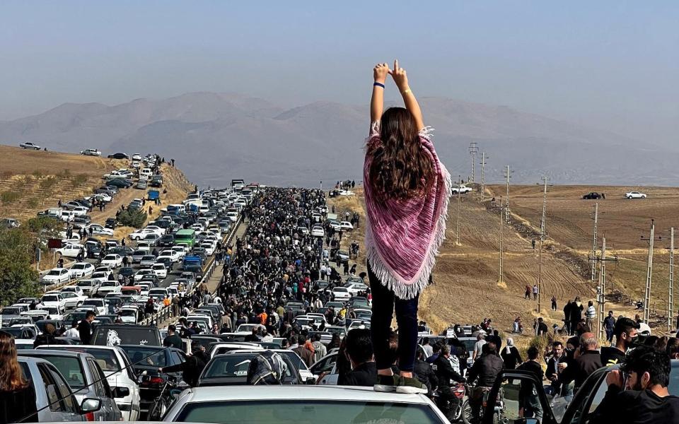an unveiled woman standing on top of a vehicle as thousands make their way towards Aichi cemetery in Saqez, Mahsa Amini's home town in the western Iranian province of Kurdistan, - UGC/AFP via Getty Images