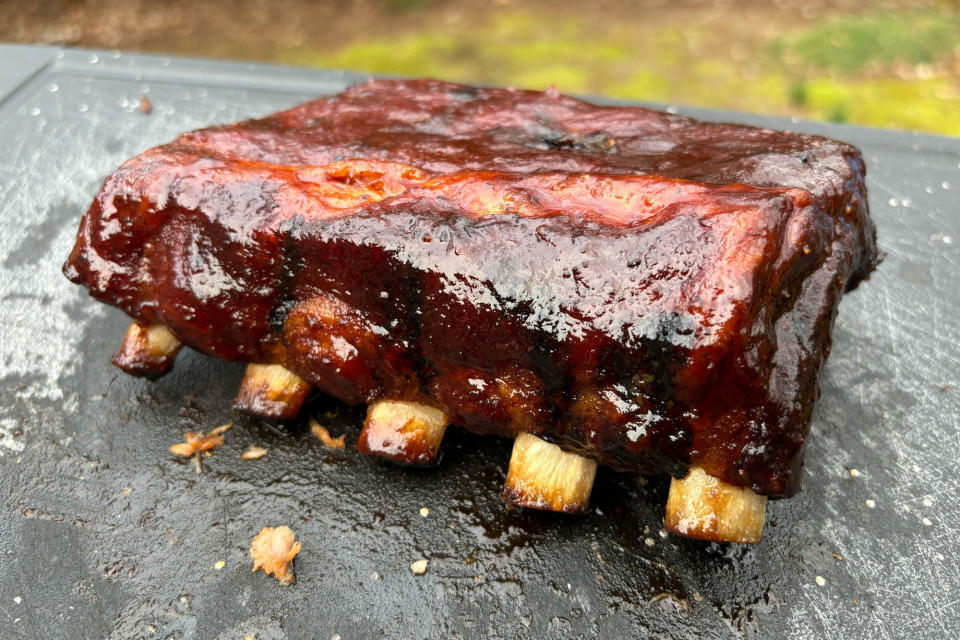 <p>Sauced baby back ribs sitting on a black cutting board.</p>
