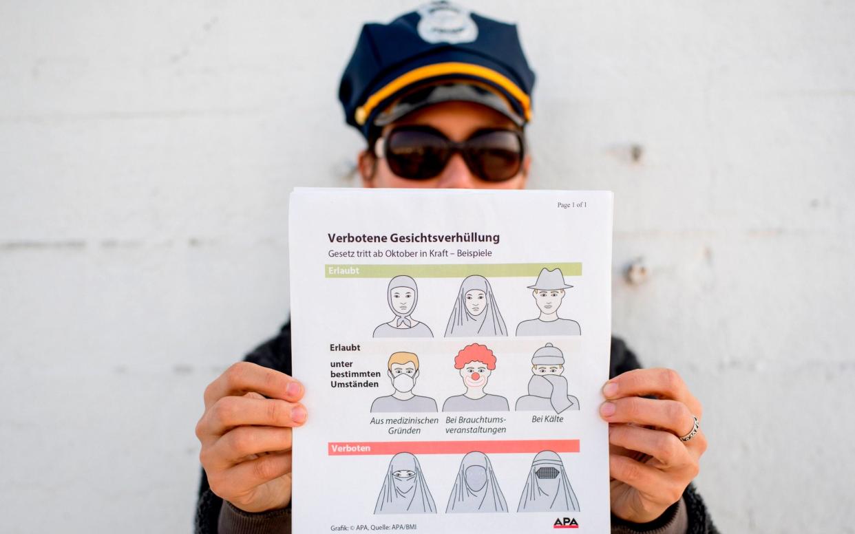 A model holds up an information pamphlet about new Austrian restrictions banning the wearing of burqas and other items covering the face in public places and building - AFP