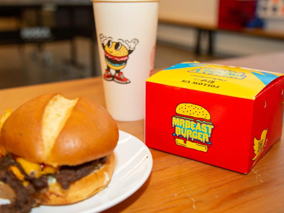 A burger on a plate next to a cup and packaging