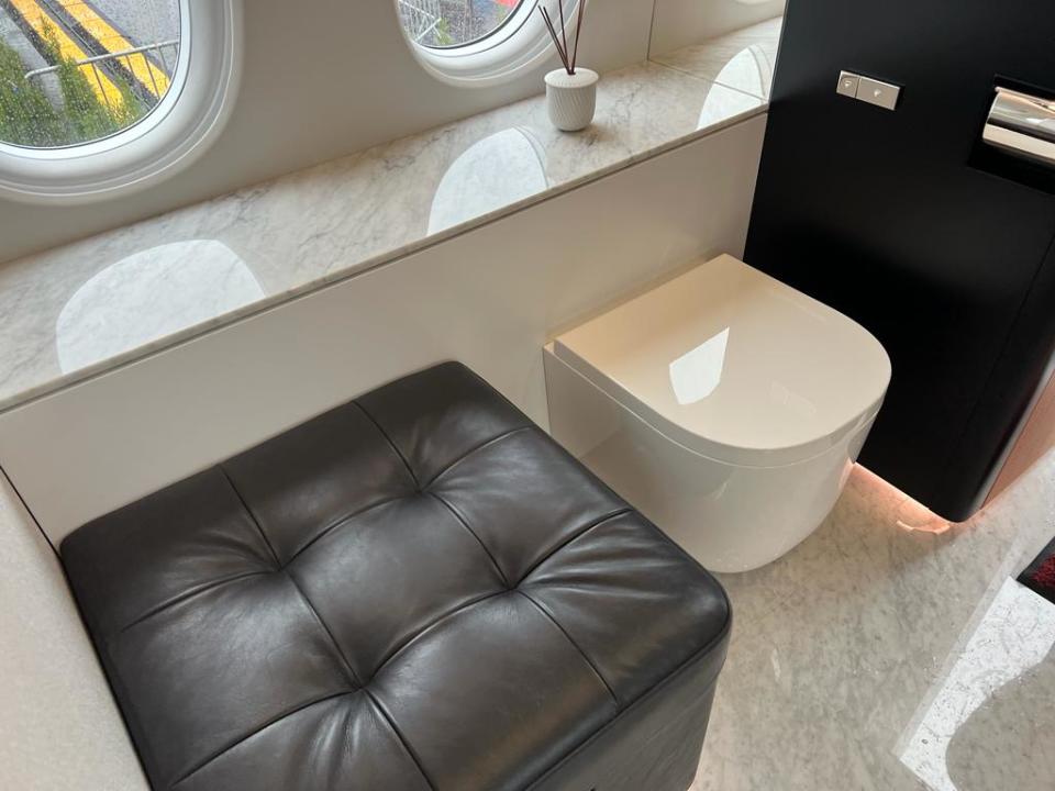 The toilet and a cushioned seat in the bathroom of a Dassault Falcon 10X, with marble floor.