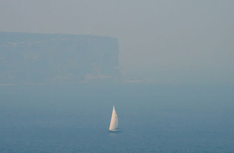FILE PHOTO: A sailing boat is seen through smoke haze from bushfires in front of the cliffs of North Head, Sydney Harbour