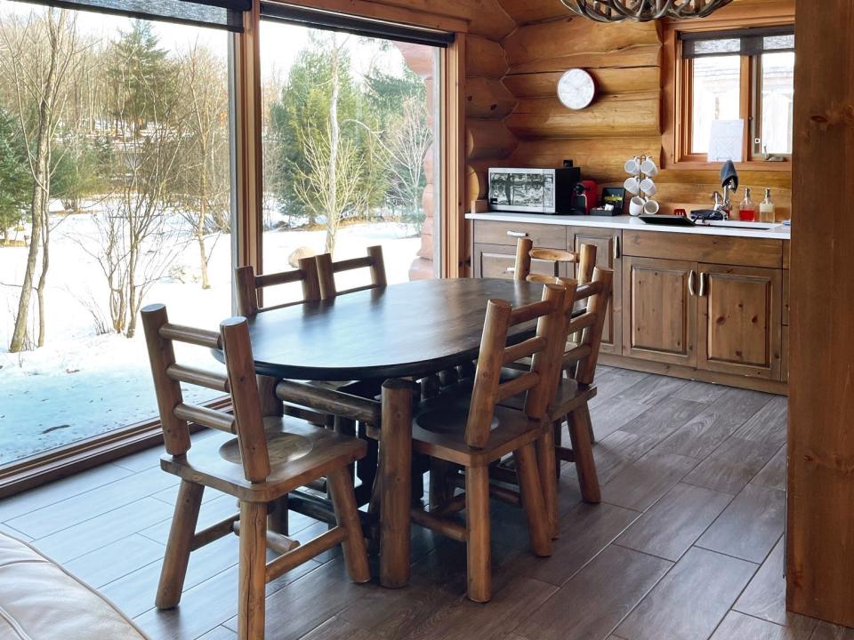 The interior of a lodge with a wooden table set, a wooden kitchen, and a deer antler light fixture hanging above counter