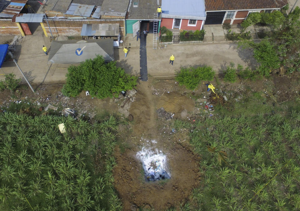 Forensic teams work to exhume several clandestine graves in Chalchuapa, El Salvador, Wednesday, May 19, 2021. The search at the home of a former policeman arrested last week for the murder of two women has turned up 10 other bodies, prosecutors said Friday, revealing the existence of a murder ring that allegedly killed as many as 13 people. (AP Photo/Salvador Melendez)