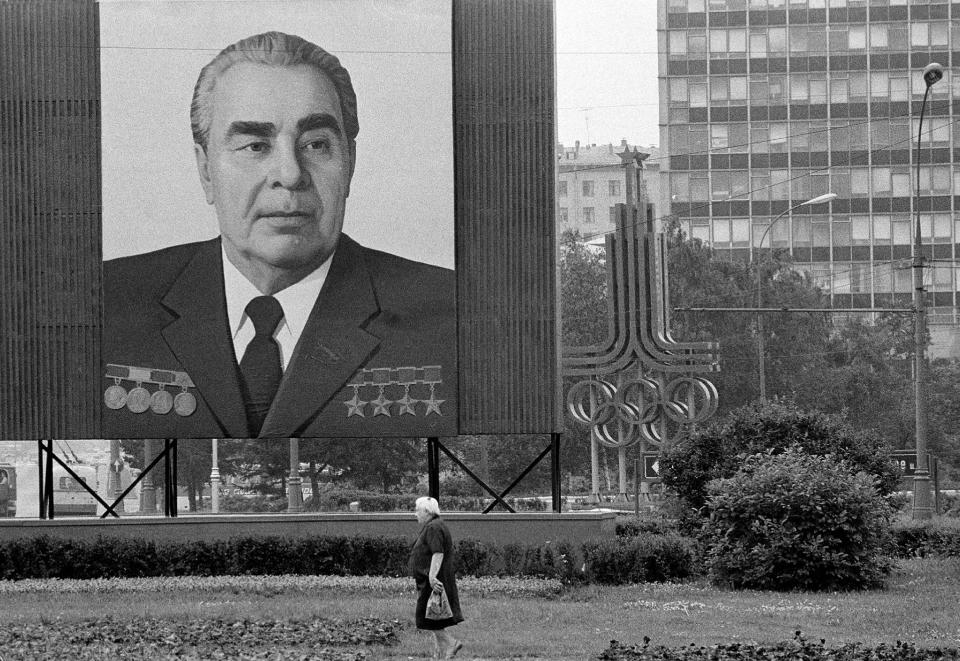 FILE - In this July 7, 1980 file photo, a woman walks past a huge portrait of Communist Party leader Leonid Brezhnev that dwarfs the symbol of the upcoming XXII Summer Olympics right behind, in Moscow. Brezhnev and his ruling Politburo wanted the games to legitimize the Soviet system, a military superpower and economic basket case. (AP Photo/File)