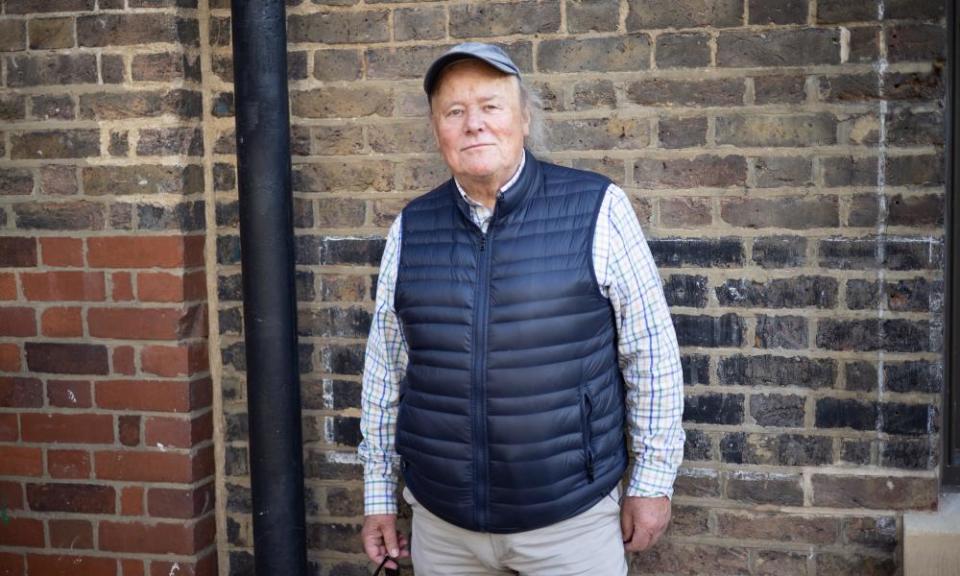 Portrait of Richard Norton-Taylor at home in outdoor clothes and a cap