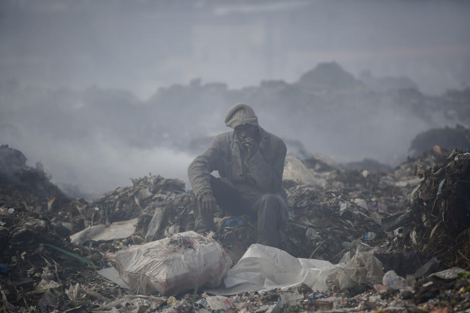 FILE - A man who scavenges recyclable materials for a living rests to smoke a cigarette on a mountain of garage amidst smoke from burning trash at Dandora, the largest garbage dump in the capital Nairobi, Kenya, Tuesday, Sept. 7, 2021. The U.N. health agency said Monday, April 4, 2022, nearly everybody in the world breathes air that doesn’t meet its standards for air quality, calling for more action to reduce fossil-fuel use, which generates pollutants that cause respiratory and blood-flow problems and lead to millions of preventable deaths each year. (AP Photo/Brian Inganga, File)