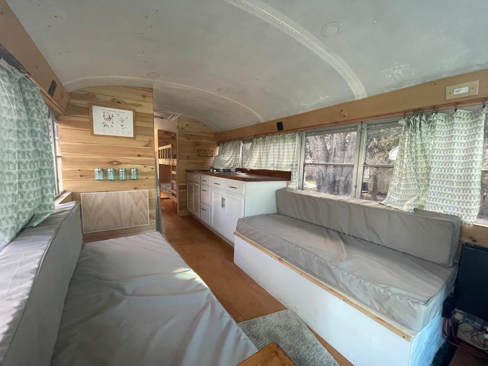 Inside of re-designed bus with gray seating, wood panelling, green curtains, and white ceiling