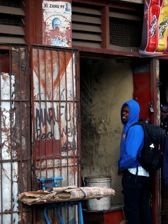 A man waits outside a groceries shop, near to a torn poster depicting late former Zimbabwe's President Robert Mugabe, in Mbare twonship, Harare