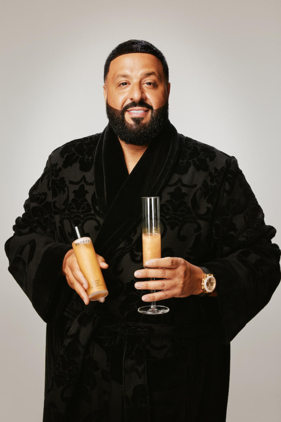 DJ Khaled in a black robe holding Aurezzi Mouthwash and a champagne flute filled with Aurezzi Mouthwash