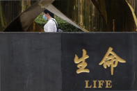 A woman wearing a face mask to help protect against the coronavirus walks by a sculpture on display on a park in Beijing, Thursday, Aug. 6, 2020. China's biggest recent outbreak of coronavirus has grown slightly. Hundreds people have developed COVID-19 in the far northwestern region of Xinjiang, with more than dozens of new cases reported Thursday in its capital and largest city, Urumqi. (AP Photo/Andy Wong)