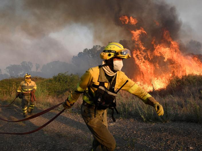 Two firefighters stand in front of a blaze.