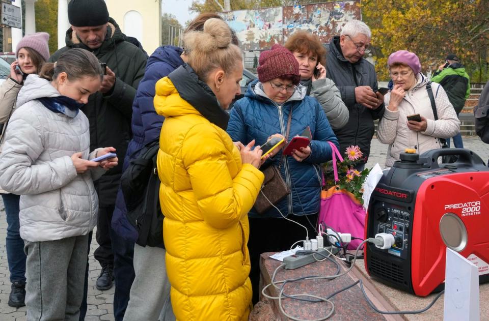 Des civils partagent un générateur pour recharger leurs téléphones à Kherson, en Ukraine, alors que les Russes en retraite bombardent les alimentations électriques (AP)