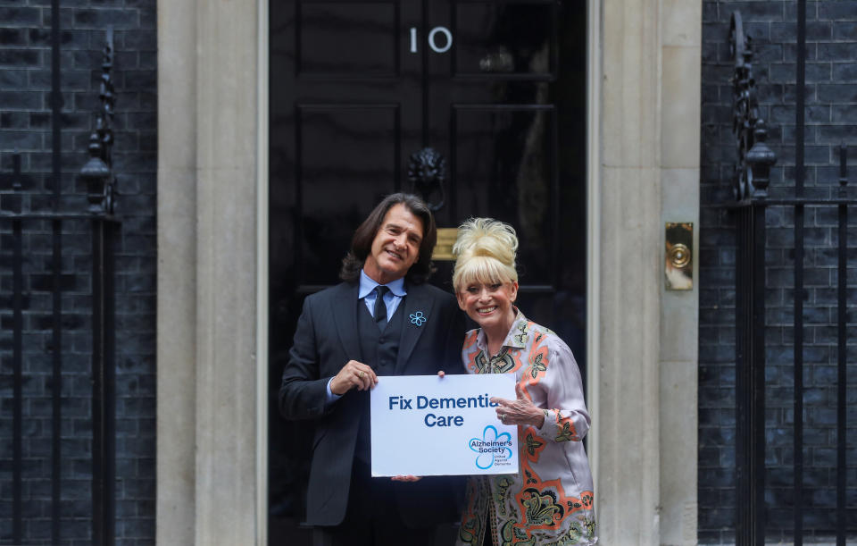 LONDON, ENGLAND - SEPTEMBER 02: Television actor Barbara Windsor and her husband Scott Mitchell pose with a placard in front of Downing Street ahead of a meeting with Britain's Prime Minister Boris Johnson in London on September 2, 2019 in London, England. Barbara Windsor, who suffers from Alzheimers, met with the Prime Minister at 10 Downing Street to discuss dementia care. (Photo by Simon Dawson - WPA Pool/Getty Images)