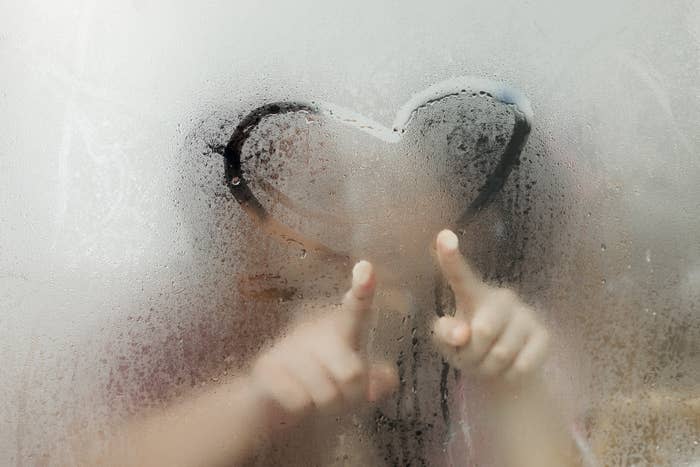 Two people drawing a heart on a foggy glass surface with index fingers