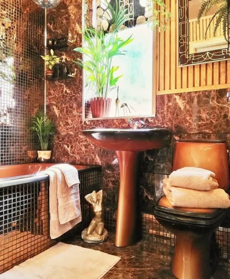 A plant filled bathroom with matching toilet and sink with mirrored tile tub