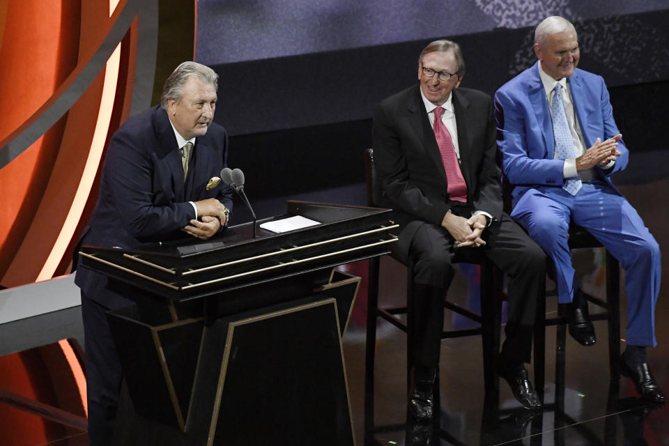 Bob Huggins speaks during his enshrinement at the Basketball Hall of Fame as presenters Rod Thorn and Jerry West, right, listen Saturday, Sept. 10, 2022, in Springfield, Mass. (AP Photo/Jessica Hill)