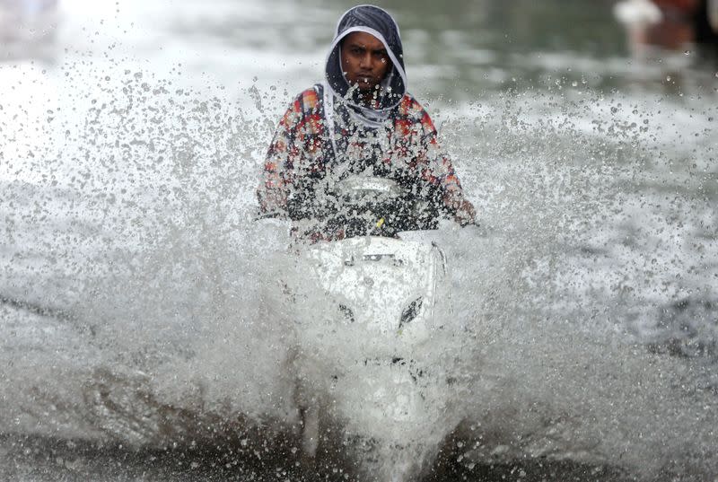 A person rides a scooter through a waterlogged road during monsoon rain showers in Mumbai