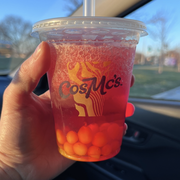 My hand holds a CosMc's plastic cup filled with a Sour Cherry Energy Burst drink.