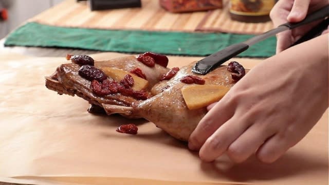 Putting cooked duck legs onto baking paper with tongs