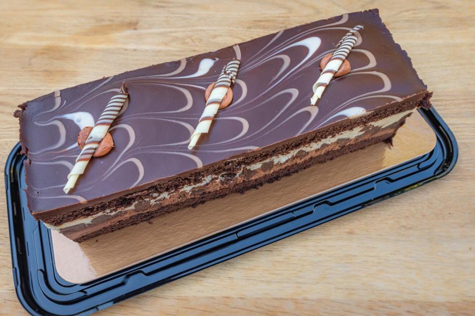 Rectangular chocolate layer cake on a plastic lid topped with swirls and white chocolate curls