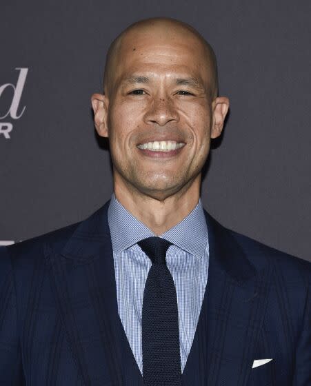 Vladimir Duthiers smiling in a dark blue suit and tie against a black background