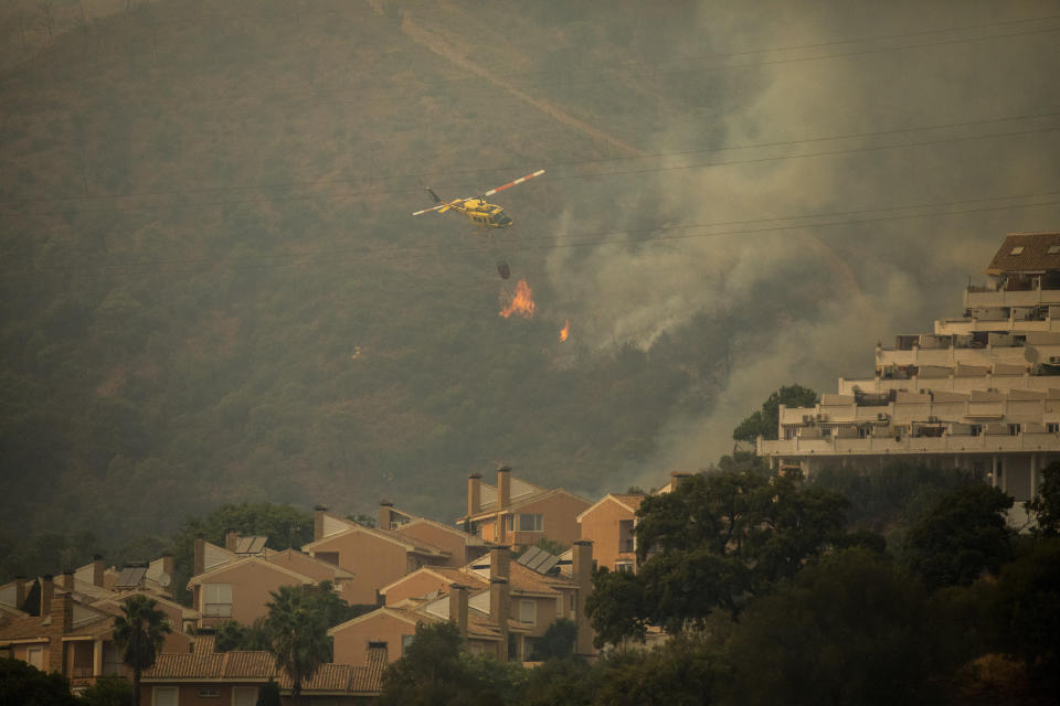 A helicopter makes a water drop over a wildfire in Estepona, Spain, Thursday, Sept. 9, 2021. Nearly 800 people have been evacuated from their homes and road traffic has been disrupted as firefighting teams and planes fight a wildfire in southwestern Spain. (AP Photo/Sergio Rodrigo)