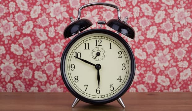 An old fashioned alarm clock in front of floral patterned wallpaper