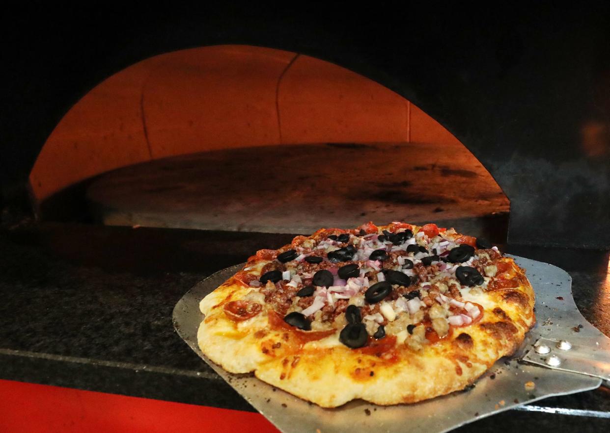 A Royal Feast pizza, made with pepperoni, sausage, bacon, onions, olives, basil and shaved parmesan, comes out of the brick oven in the kitchen of Kittle's Brick Oven Pub in Green.