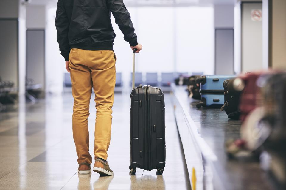 Low Section Of Young Man With Luggage Standing By Conveyor Belt At Airport