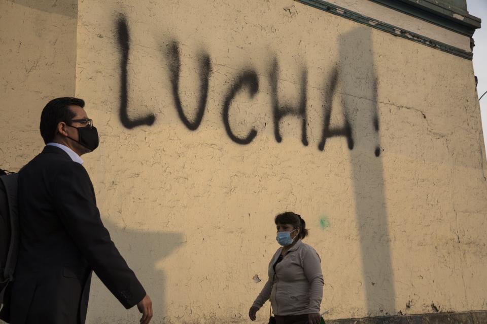 Pedestrians walk past a wall spray-painted by an anti-government protester with the Spanish word for fight, just a block from the Justice Palace where people who are refusing to recognize Peru's new government gathered to protest, in Lima, Wednesday, Nov. 11, 2020. On Tuesday, Peru swore in former congressional leader Manuel Merino as president, after the legislature booted President Martin Vizcarra from office on Monday. (AP Photo/Rodrigo Abd)