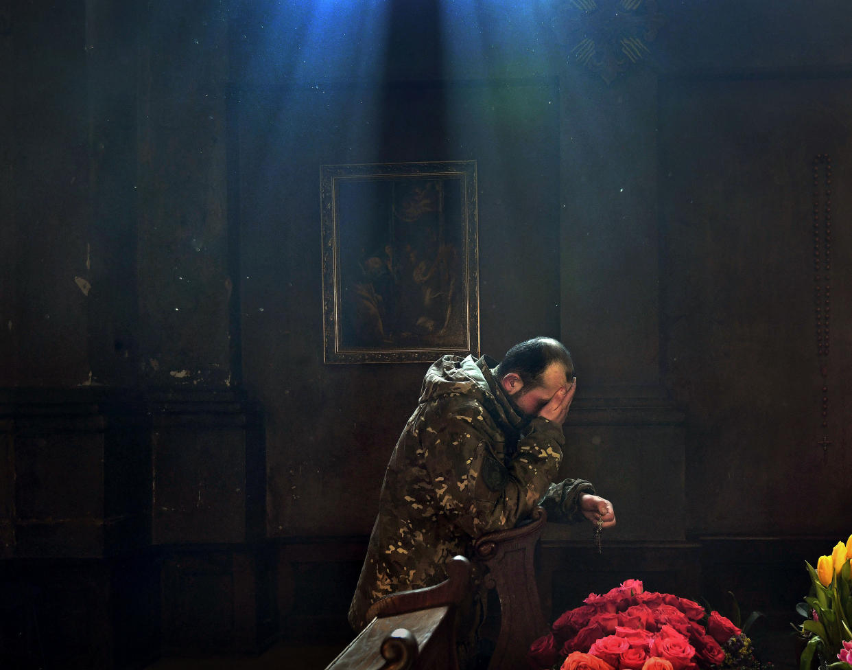 Sunlight filters through a church window and onto a Ukrainian soldier who is kneeling to pray.