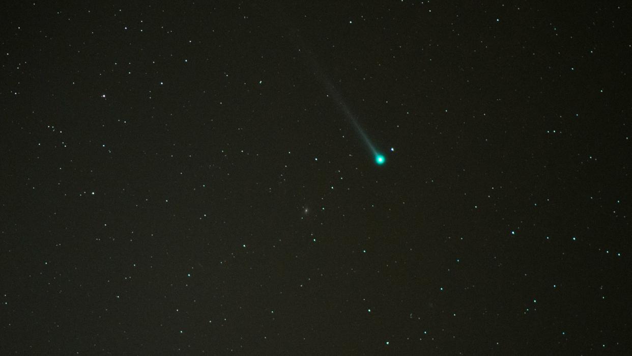  A greenish comet streaks through the night sky. 