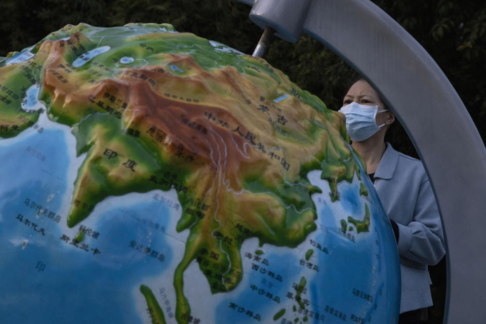 In this Wednesday, April 15, 2020, photo, a woman wearing a mask against the coronavirus looks at a globe showing China, in Wuhan in central China's Hubei province. Top Chinese officials secretly determined they were likely facing a pandemic from a novel coronavirus in mid-January, ordering preparations even as they downplayed it in public. Internal documents obtained by the AP show that because warnings were muffled inside China, it took a confirmed case in Thailand to jolt Beijing into recognizing the possible pandemic before them. (AP Photo/Ng Han Guan)