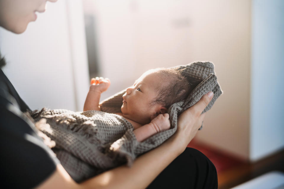 Cropped shot of a loving Asian mother holding newborn baby wrapped in a towel, drying baby girl after a fresh bath. New life. Love and care concept