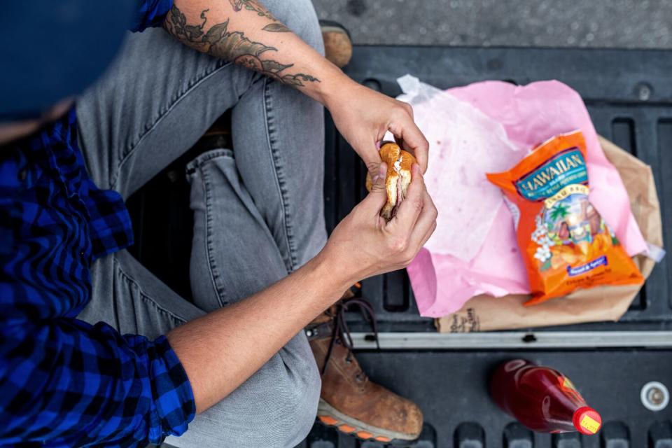 An overhead detail of Danny Palumbo holding a sandwich while sitting crosslegged on the tailgate of his truck.