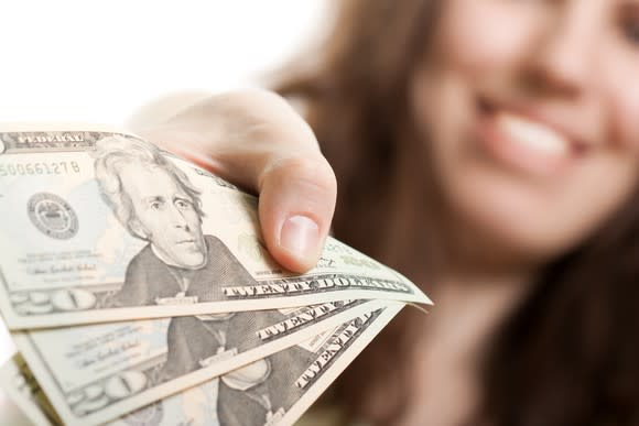 A woman holds three $20 bills.