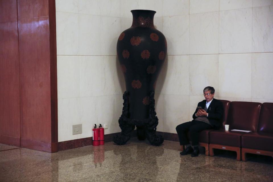 In this Friday, March 10, 2017 photo, a delegate browses his phone near a fire extinguishers and a porcelain vase during the Chinese People's Political Consultative Conference (CPPCC) at the Great Hall of the People in Beijing. Because safety comes first, fire extinguishers are ubiquitous in and around Beijing’s Great Hall of the People during the annual sessions of China’s ceremonial parliament and its official advisory body. That’s partly for standard purposes of preventing any sort of fire-related emergency that could harm the participants and mar the proceedings. (AP Photo/Andy Wong)