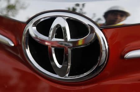 A worker is reflected next to the emblem of a Toyota Vios sedan at a stockyard of the Toyota Philippines manufacturing plant in Sta Rosa, Laguna, south of Manila August 11, 2014. REUTERS/Erik De Castro