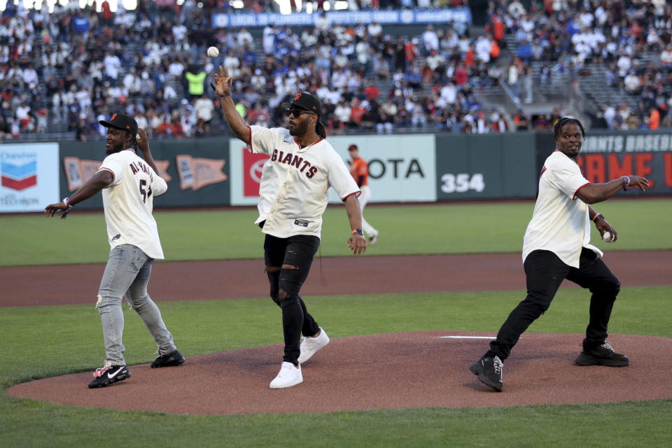 San Francisco 49ers' Azeez Al-Shaair, left, Fred Warner, center and Dre Greenlaw, right, throw ceremonial first pitches before a baseball game between the San Francisco Giants and the Los Angeles Dodgers in San Francisco, Friday, June 10, 2022. (AP Photo/Jed Jacobsohn)